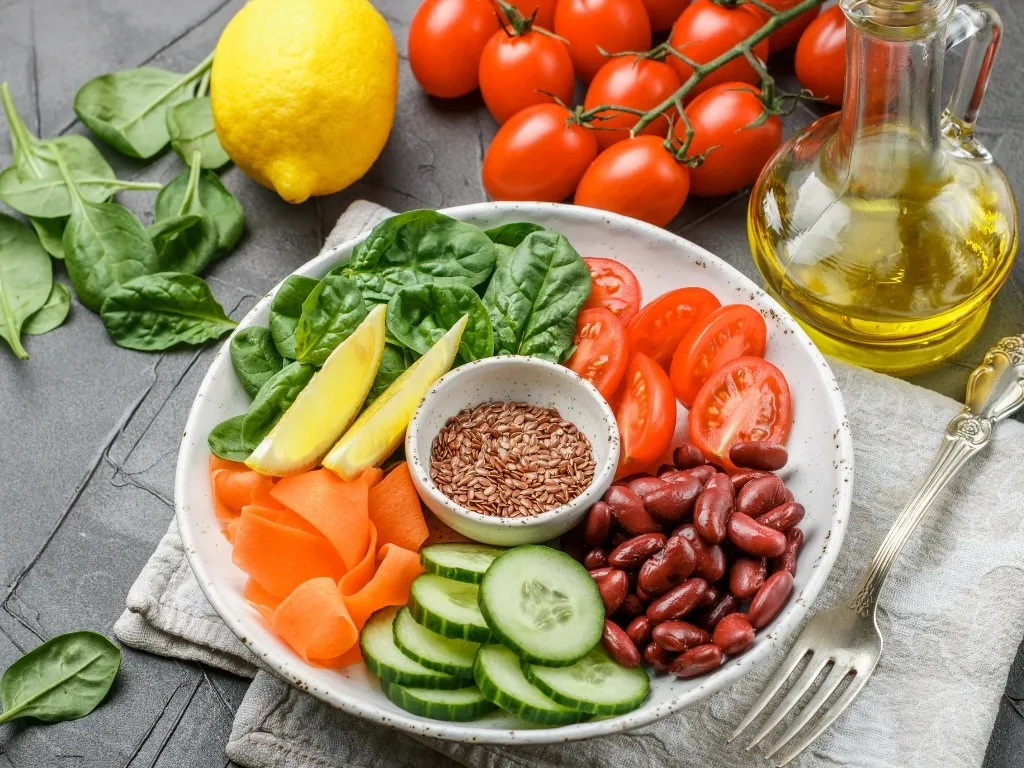 A balanced plate of spinach, cucumber, tomatoes, seeds, carrots, and lemon, surrounded by various ingredients and a fork
