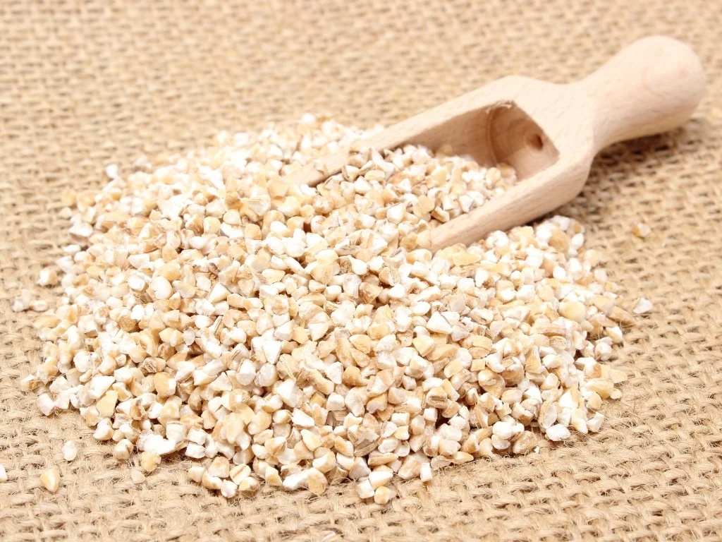 Pile of barley groats next to a wooden grain scoop