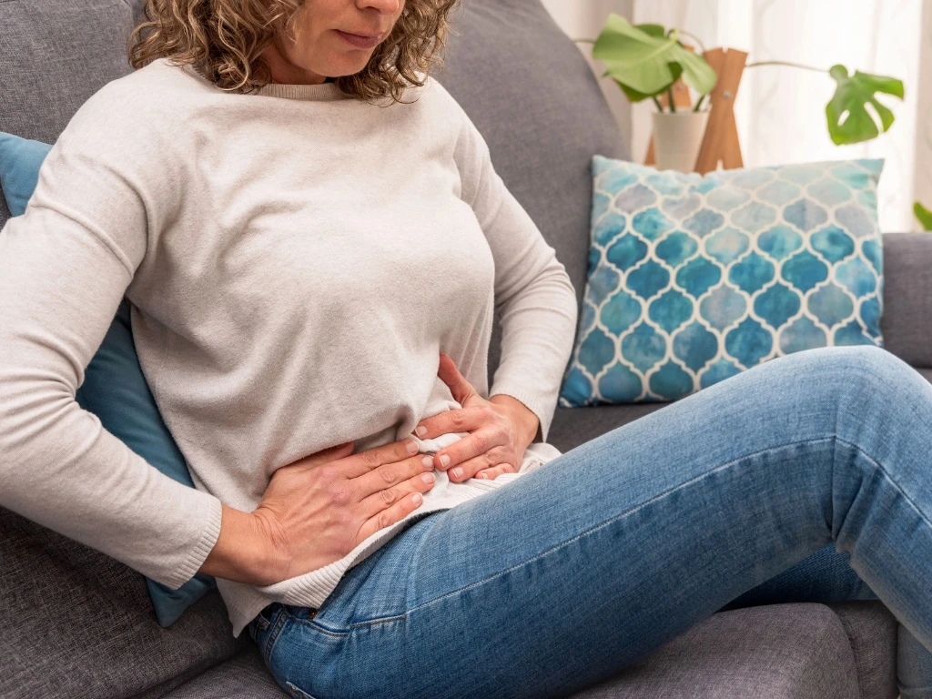 Woman experiencing abdominal pain while sitting down on a couch