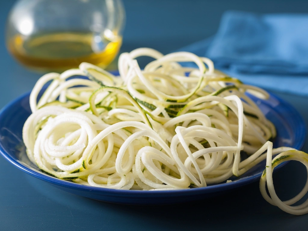 Zucchini noodles served on a blue plate, with a jar of oil in the background