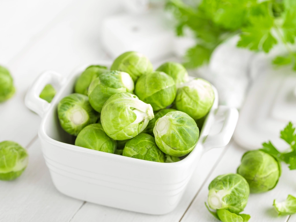 White ceramic bowl filled with fresh, green Brussels sprouts on a white wooden table