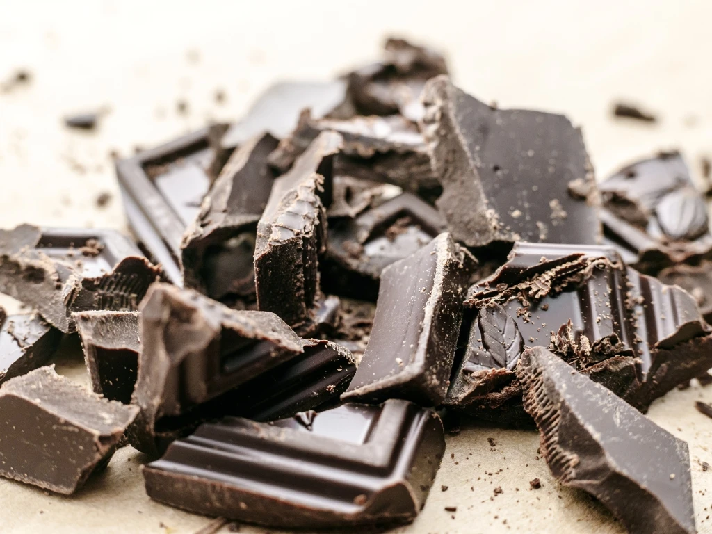 Pile of broken dark chocolate chunks and shards scattered on a light brown textured surface