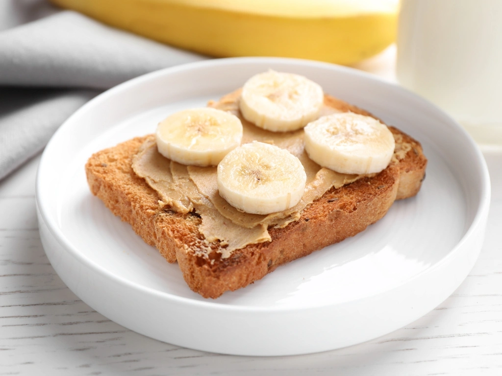 Whole-grain toast topped with peanut butter and banana slices on a white plate