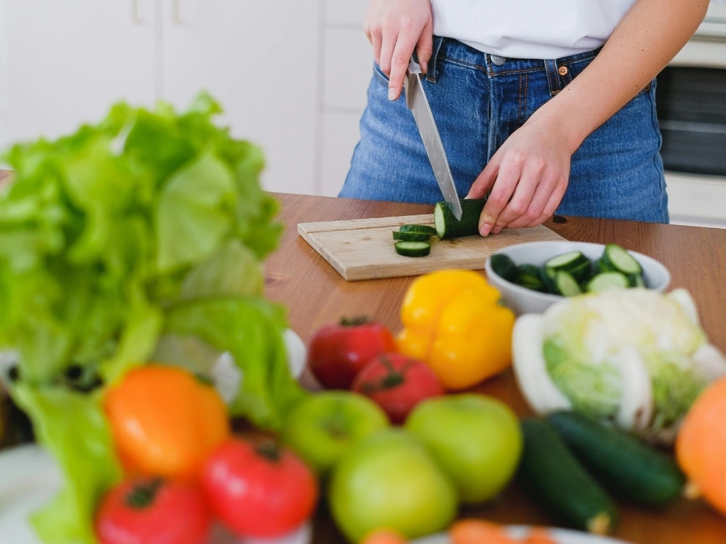 A person slicing cucumbers on a cutting board, with a variety of vegetables displayed in front