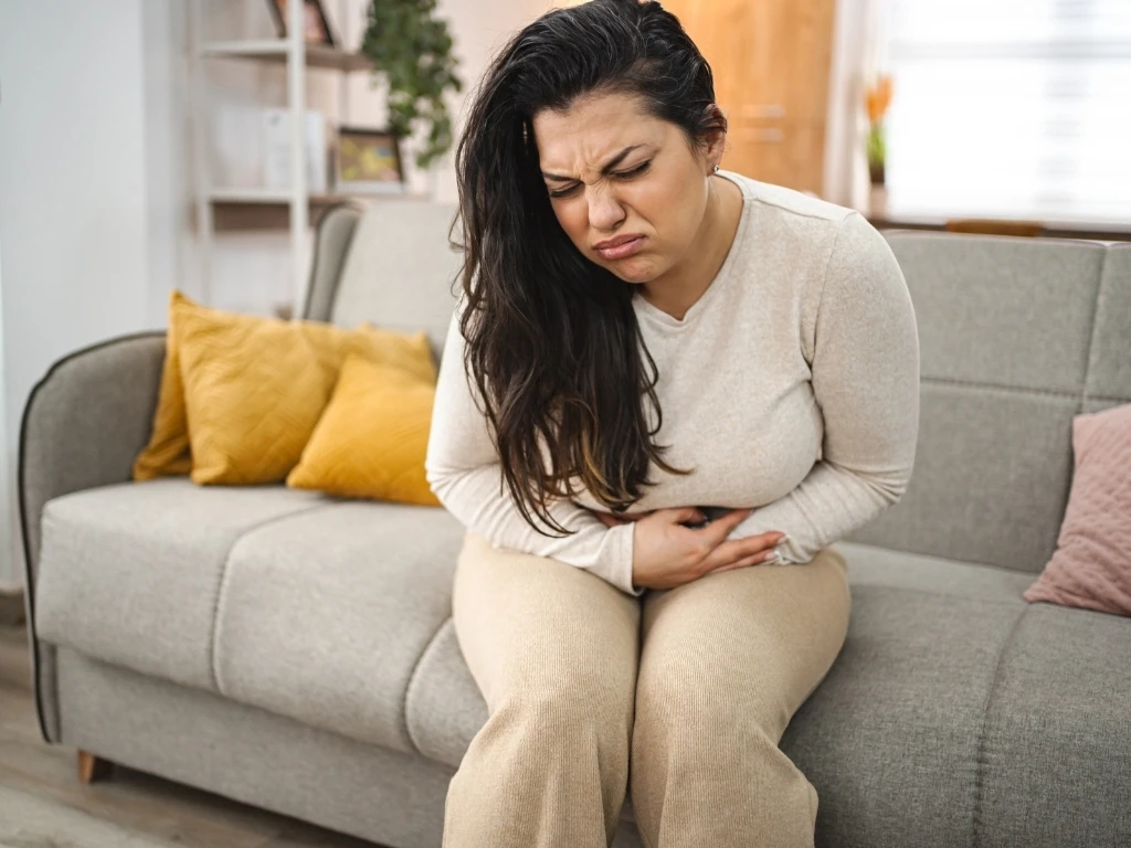A woman sitting on the couch at home, clutching her stomach in pain