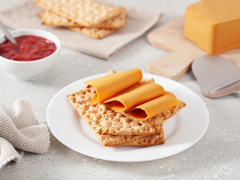 Crisp whole-grain crackers topped with thin slices of cheese, served with a side of red fruit jam