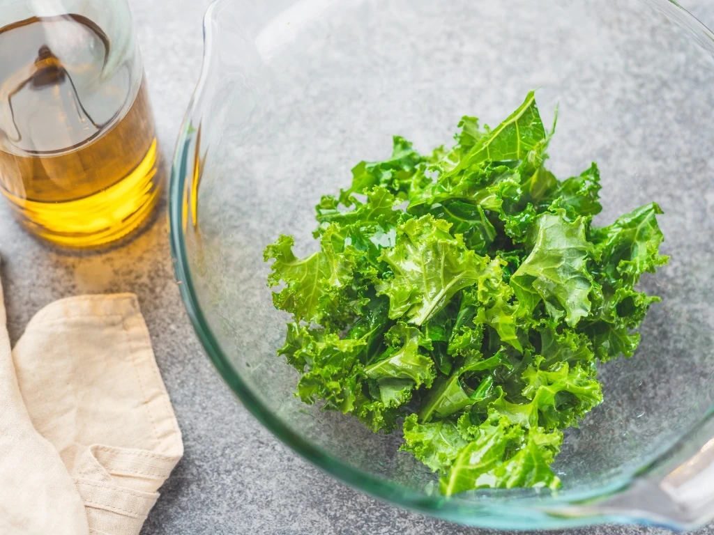 Chopped leafy greens in a bowl next to a bottle of olive oil and a tablecloth