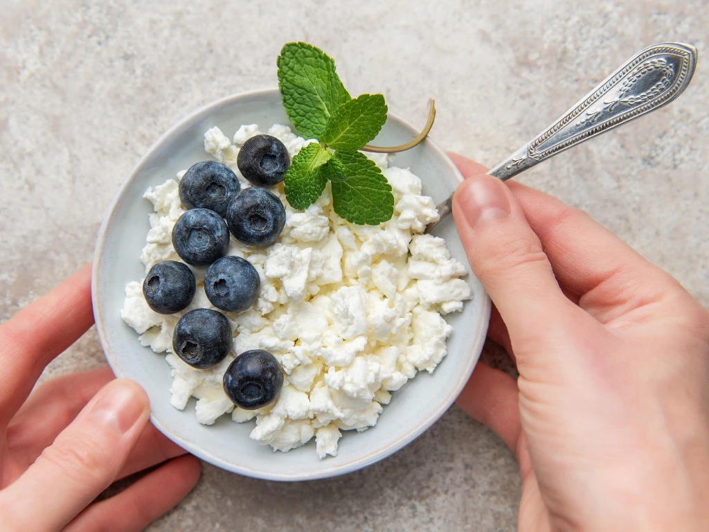 Person holding a plate of cottage cheese and blueberries