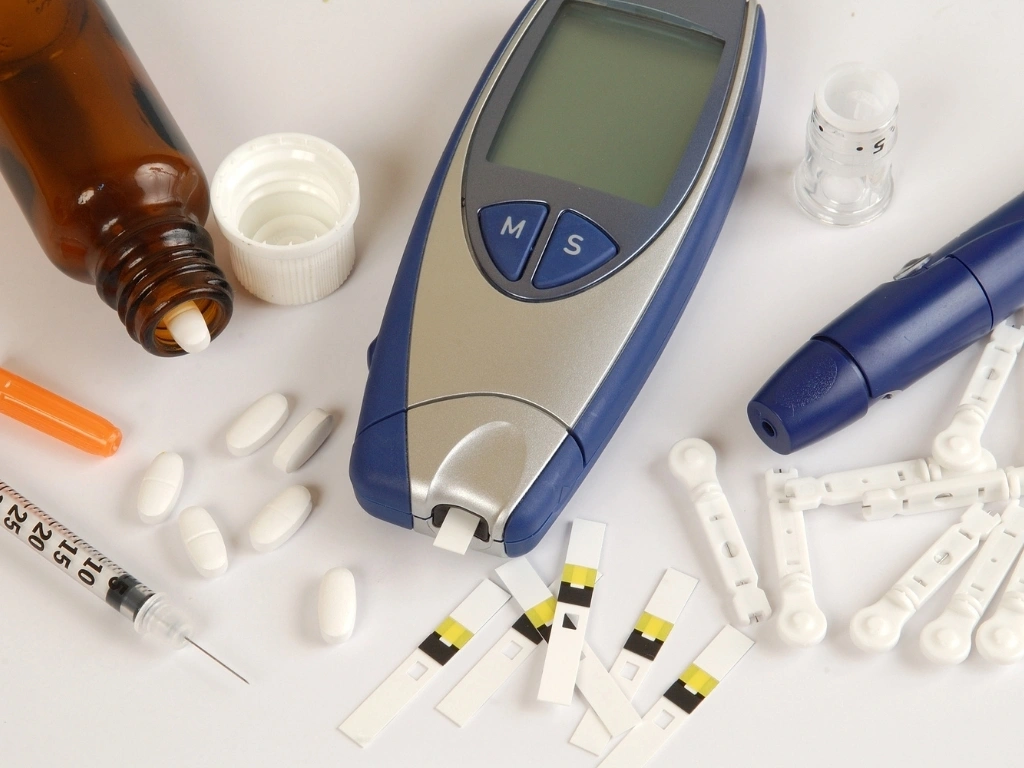 Man seated at a wooden table sorting diabetes medications in his hand, with a glass of water beside him