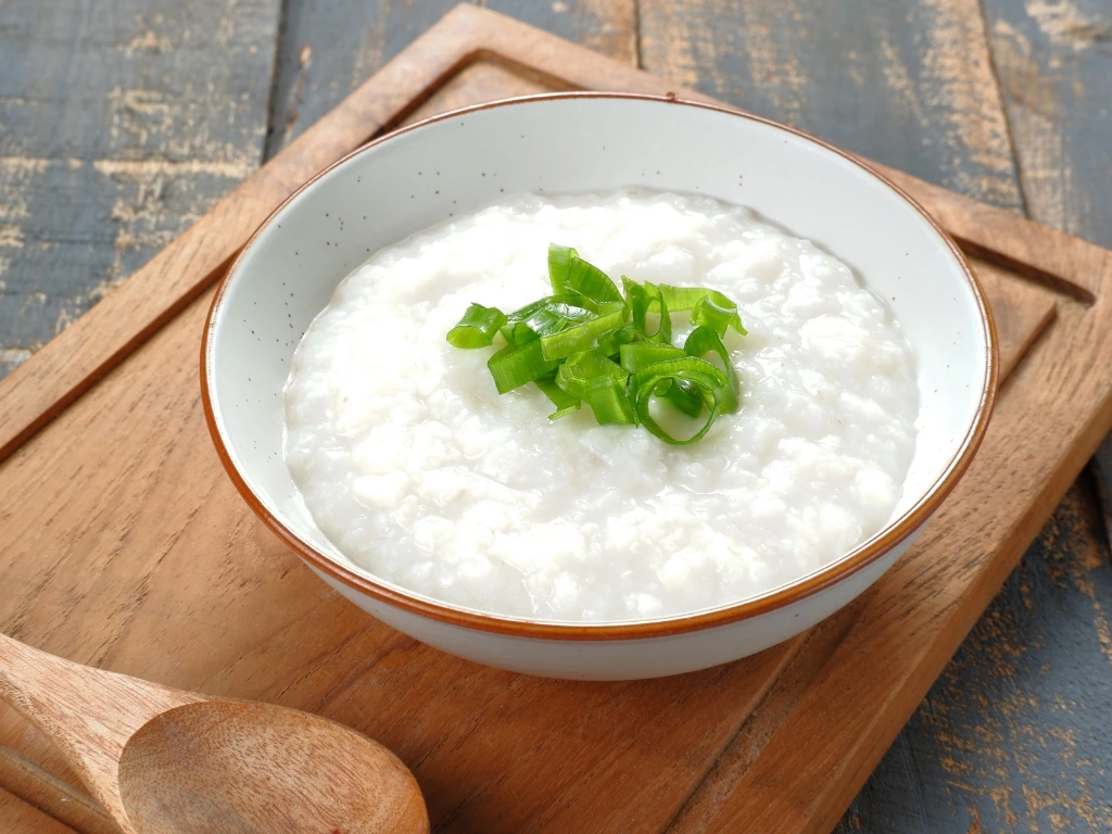Bowl of rice porridge on a wooden tray, served with a wooden spoon