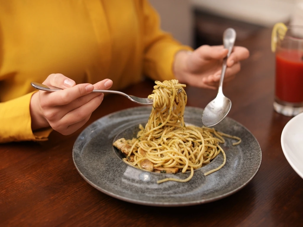 Woman in yellow eating pasta in a restaurant, with a glass of fruit juice in the background
