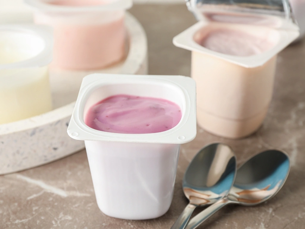 Several individual yogurt cups on a textured surface, next to two spoons