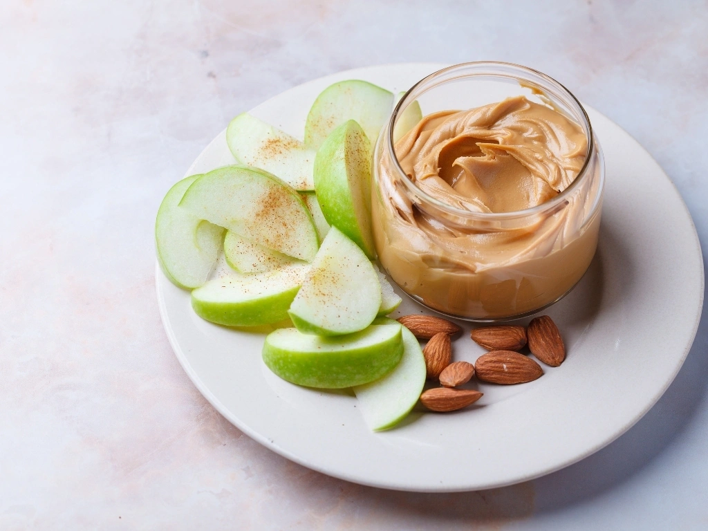 Slices of green apple sprinkled with cinnamon, served with a jar of nut butter and whole almonds