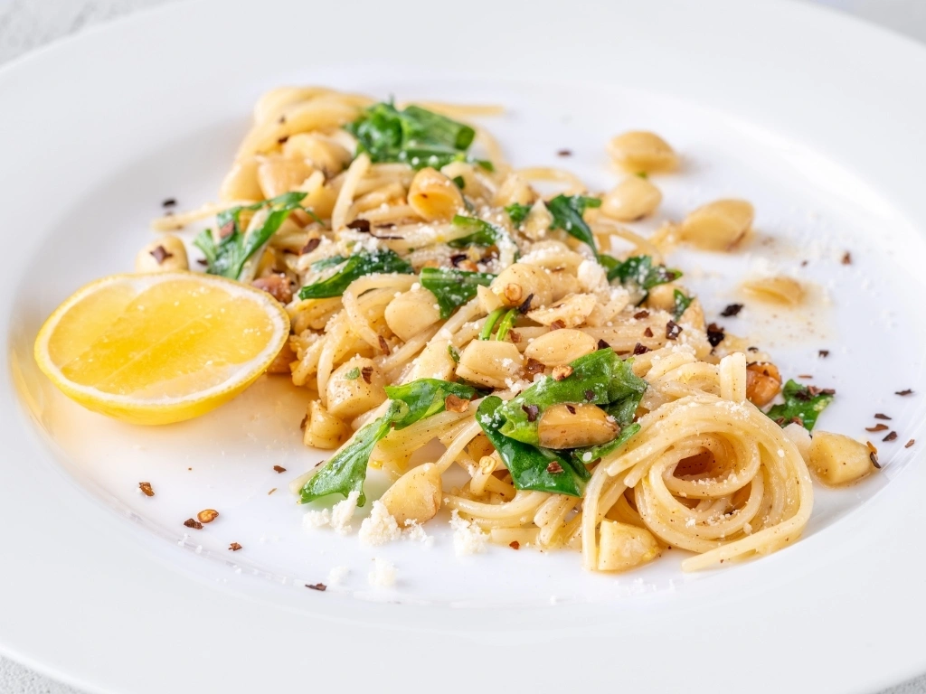 Pasta with pine nuts, greens, and chili flakes, served with a lemon wedge and grated cheese on top