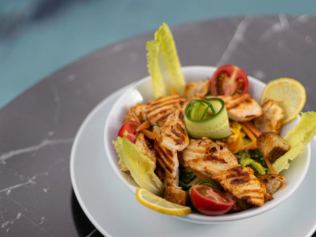 Bowl of grilled chicken salad served with a white plate on a marbled table
