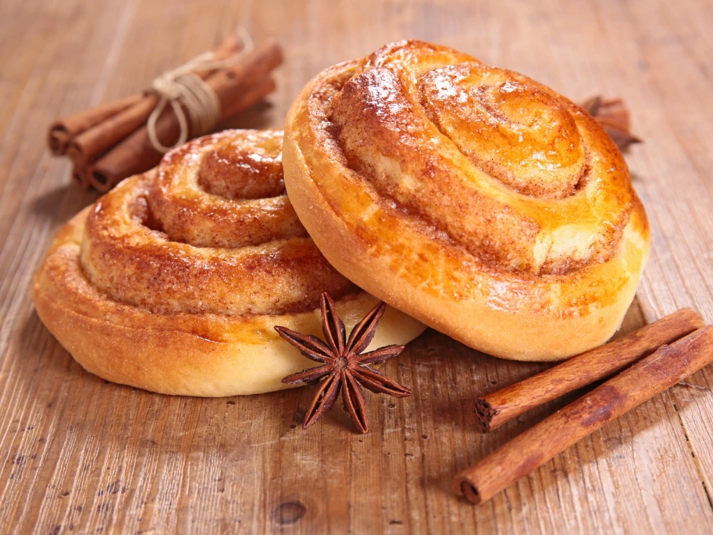Two cinnamon rolls on a wooden table alongside cinnamon sticks and star anise