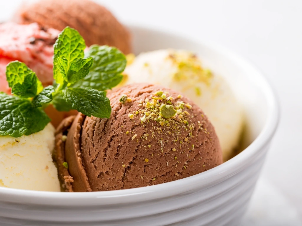White bowl filled with scoops of chocolate, vanilla and strawberry ice cream topped with pistachios and mint leaves