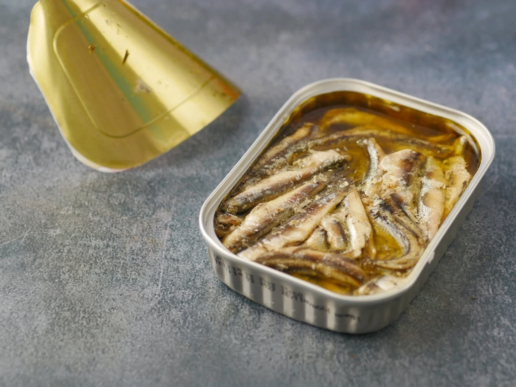 Open rectangular tin of anchovy fillets in oil with the gold lid peeled back