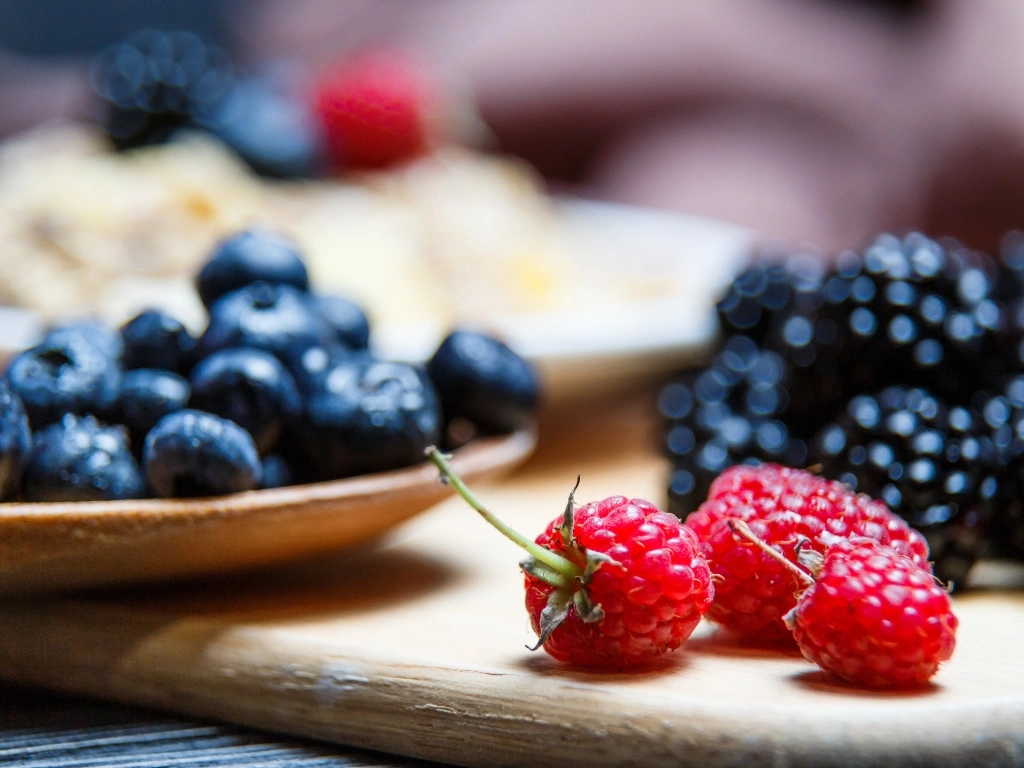 Close-up of fresh raspberries, blackberries, and blueberries arranged on a wooden board and spoon