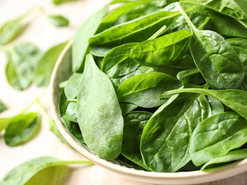 Bowl filled with fresh, green baby spinach leaves on a light-colored surface