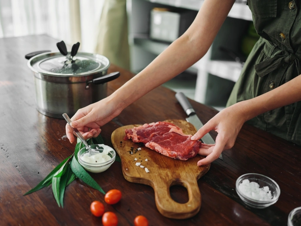 A woman seasoning red meat in the kitchen