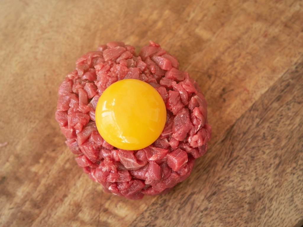 Steak tartare topped with raw egg yolk, served on a wooden surface