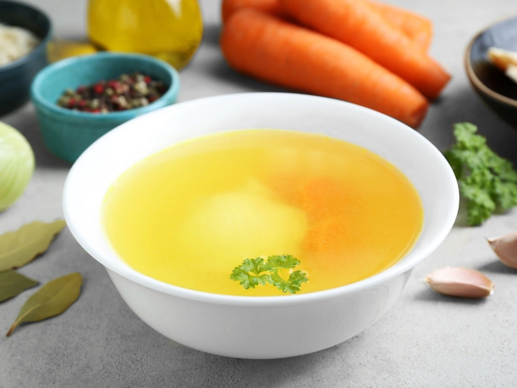 Bowl of vegetable broth with different raw ingredients in the background