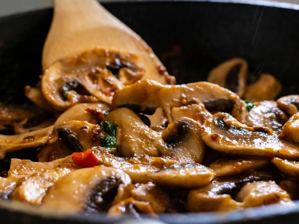 mushroom and red pepper sauce in a pan cooking with mixing wooden paddles