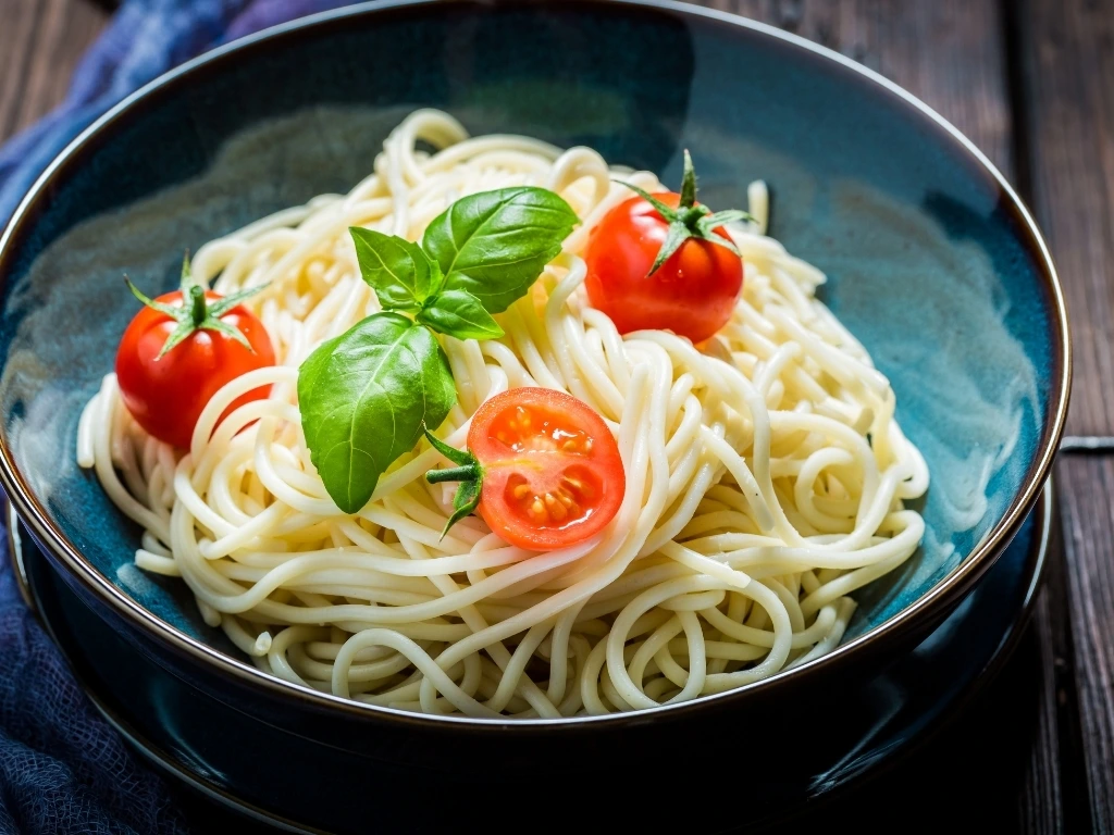 Bowl of cooked spaghetti served with tomatoes and herbs