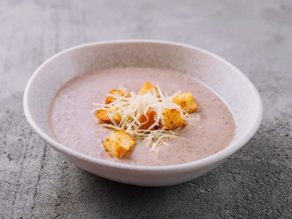 Bowl of creamy soup topped with croutons and parmesan cheese