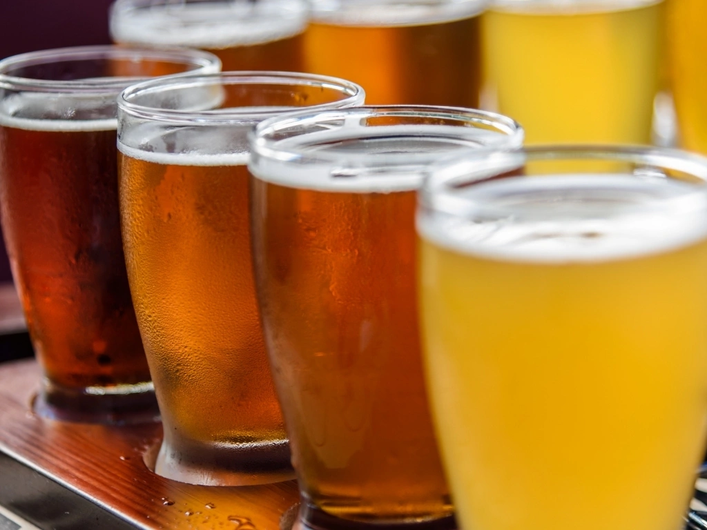 Four glasses of beer in a row, with more in the background