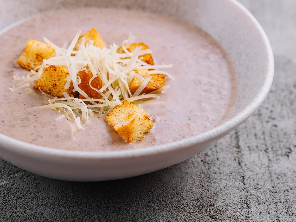 Bowl of creamy soup topped with croutons and parmesan cheese