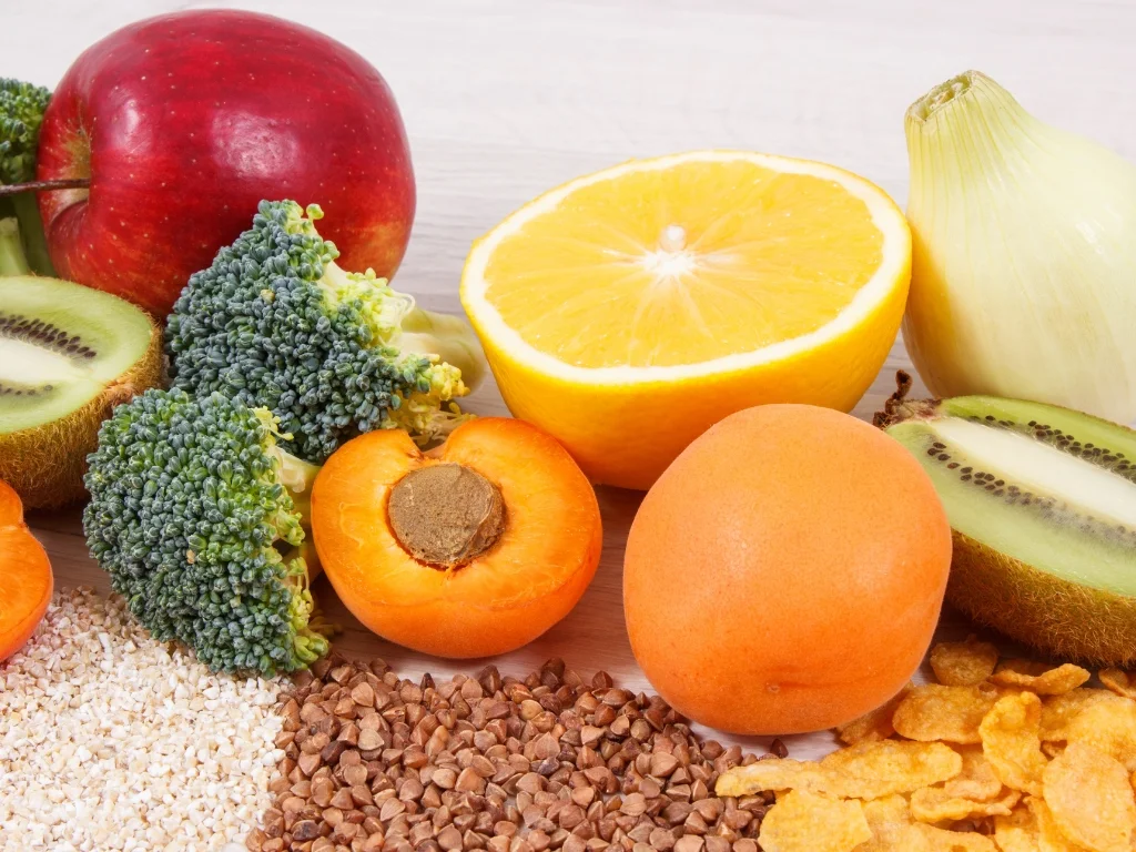 Assortment of high-fiber fruits, vegetables, grains, and cornflakes on a wood-like surface