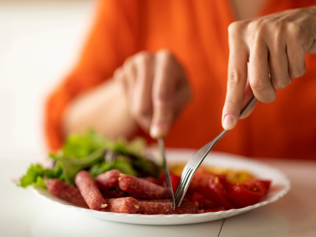 Woman eating a plate of sausages and vegetables