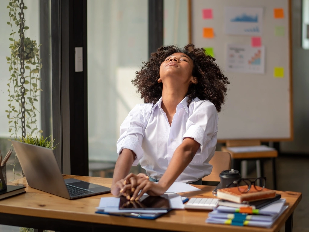 Woman sitting by the table with her eyes closed, taking a short break from using her laptop for work