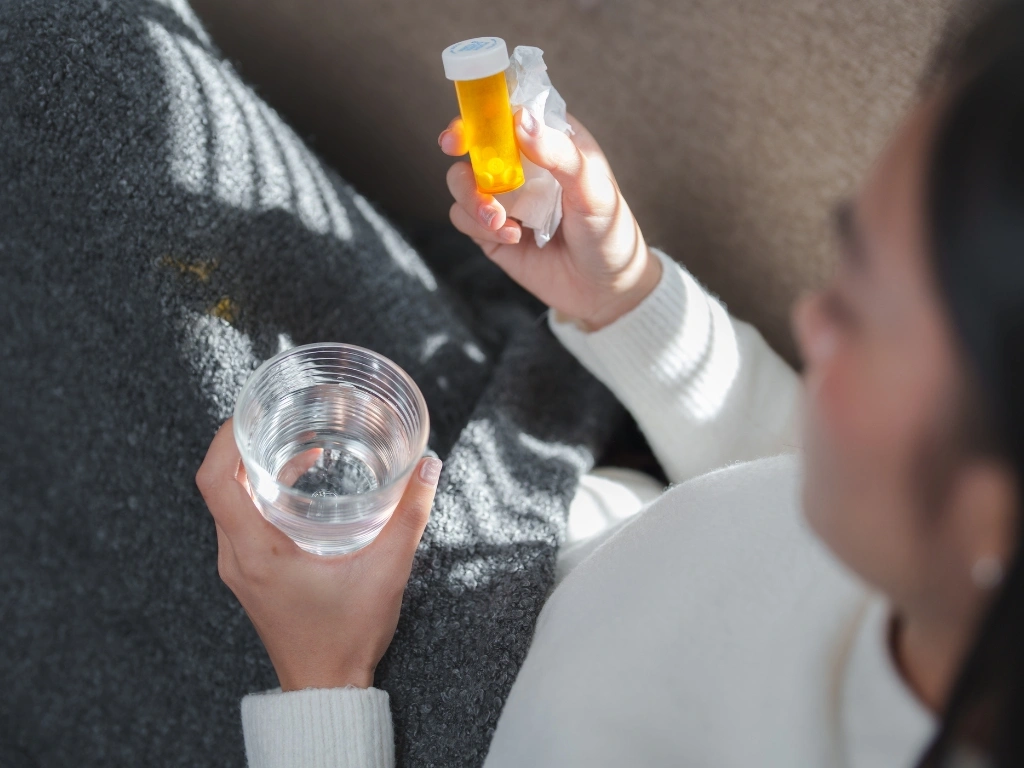Woman holding a medicine bottle with white round pills in one hand and a glass of water in the other