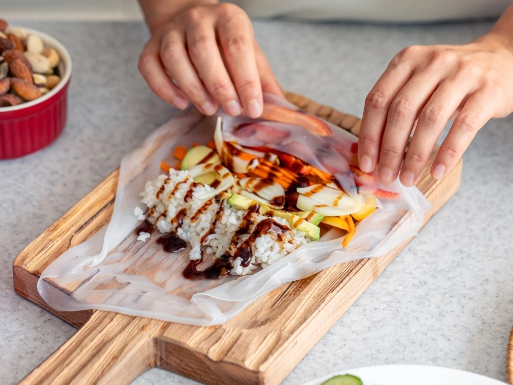 Person preparing rice paper vegetables rolls on a wooden board