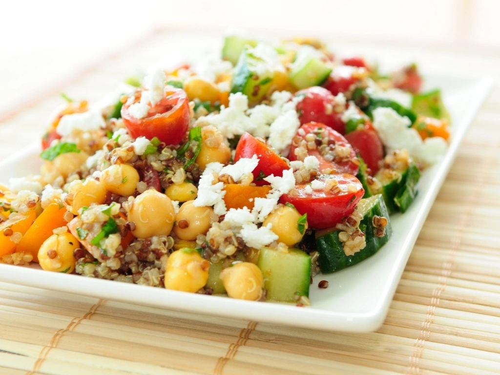 Rectangular plate of quinoa and chickpea salad with cucumber, tomatoes, and cheese