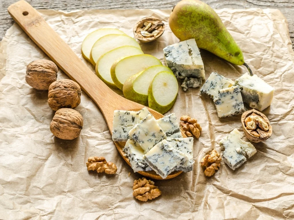Walnuts, blue cheese, sliced pears, and a wooden spoon spread on top of parchment paper