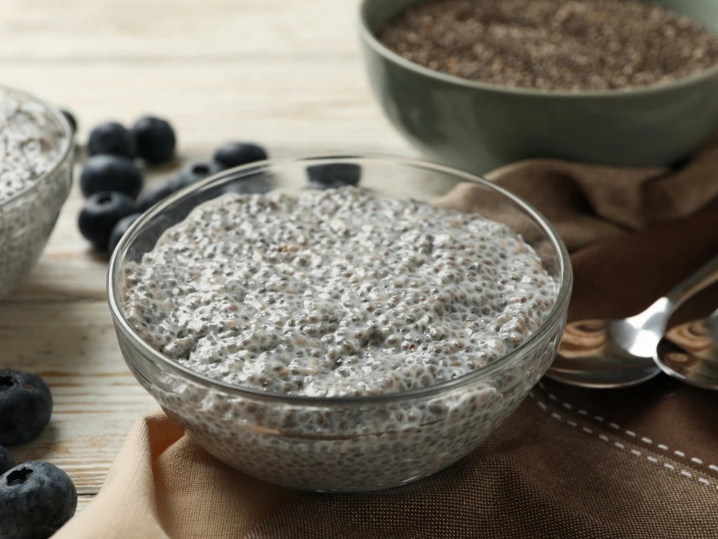 Plain chia pudding served in a bowl, with spoons and ingredients across the table