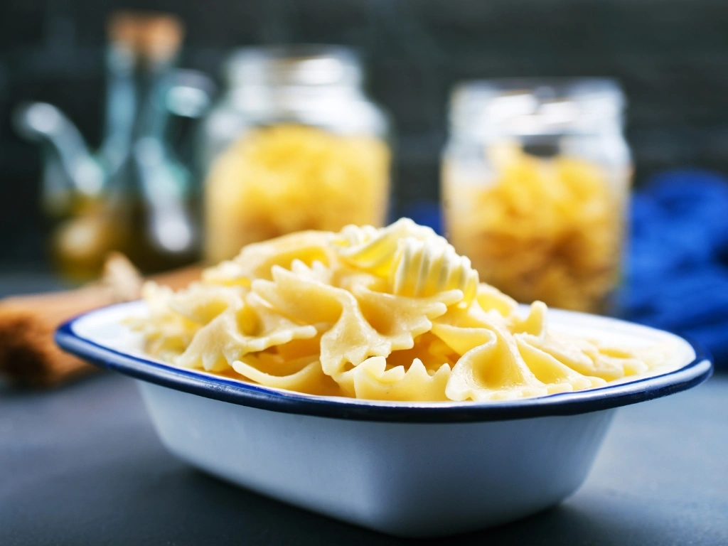 White enamel dish of cooked farfalle pasta with blurred jars in the background