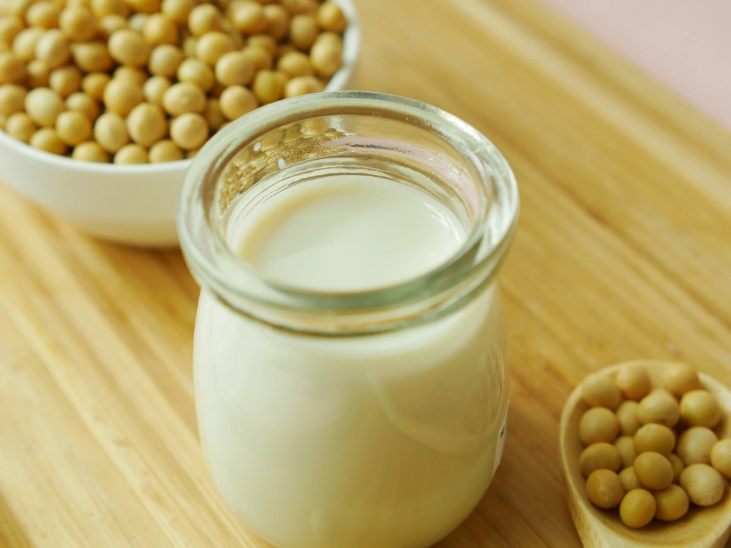Glass jar of soy milk on a wooden board next to bowls of soybeans