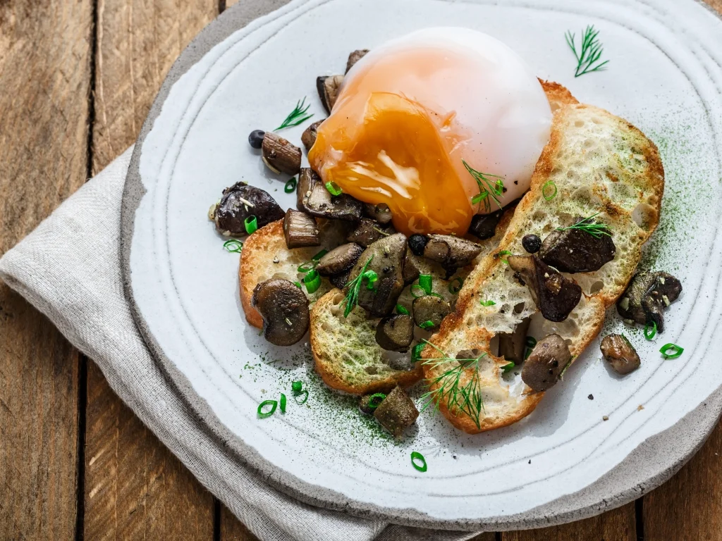 Soft poached egg with a runny yolk served over sautéed mushrooms and toasted bread on a plate