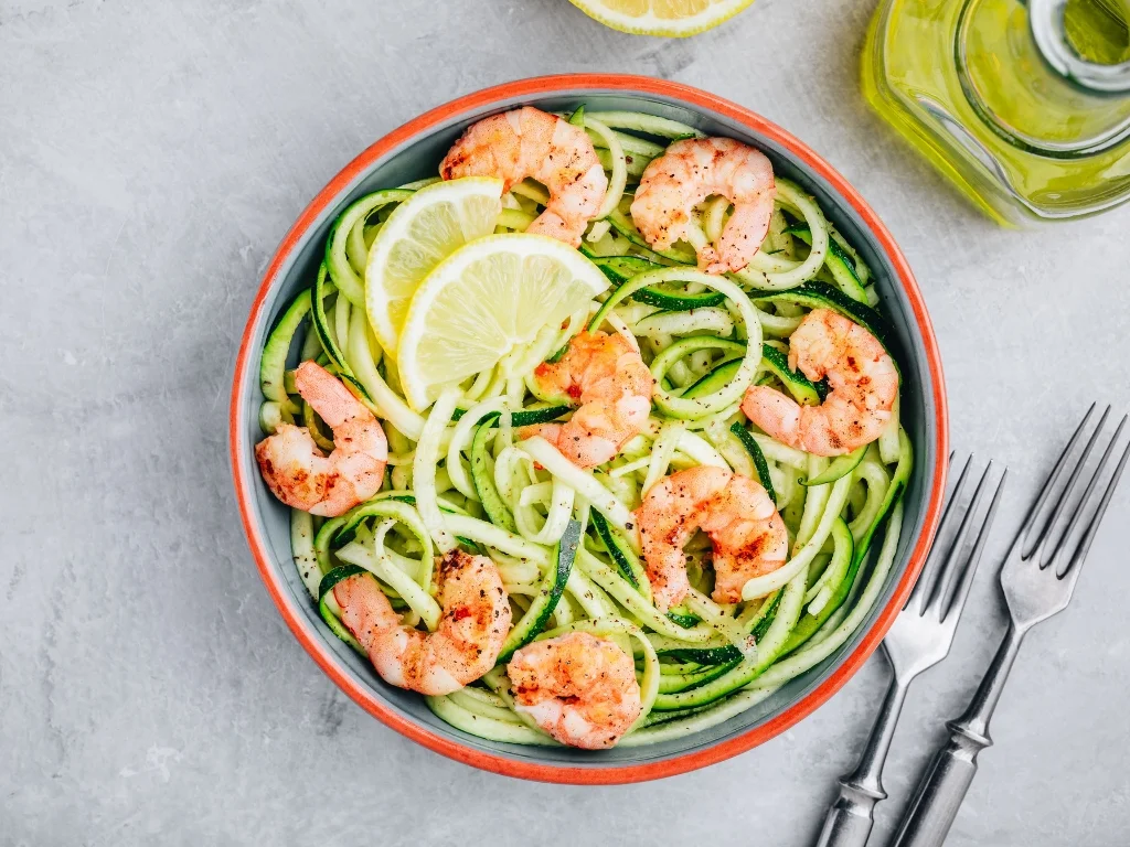 Garlic shrimp and lemon wedges on zucchini noodles, served next to a jar of olive oil and two forks