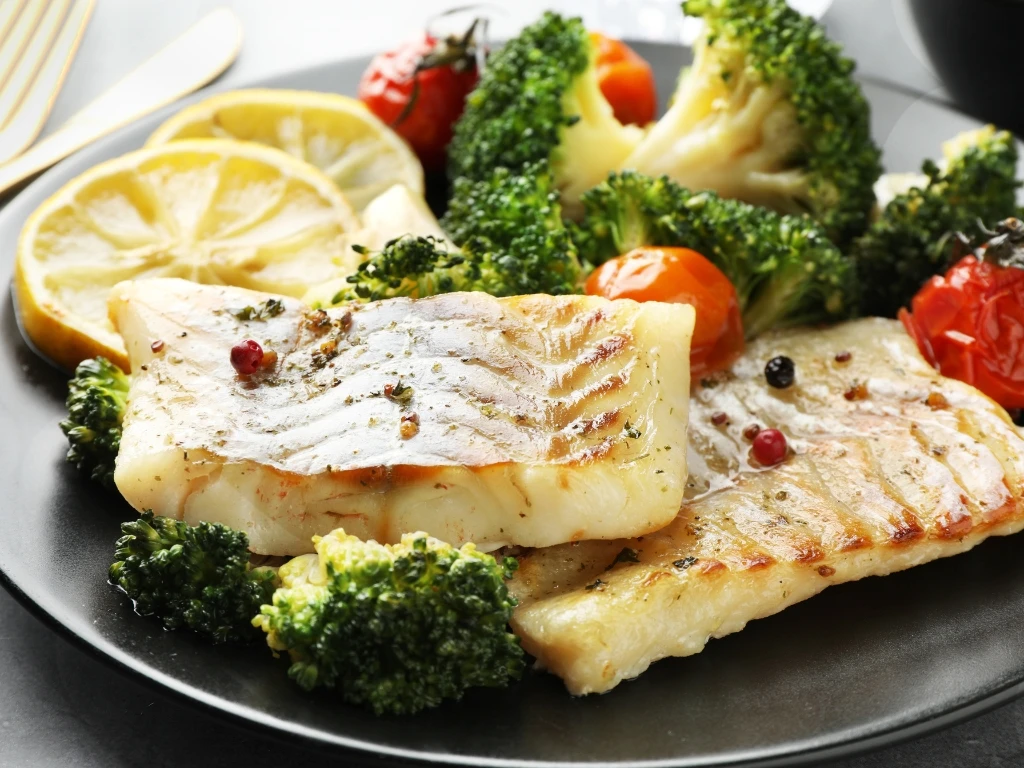 Baked cod with broccoli, roasted tomatoes, and lemon slices, served on a plate with a fork