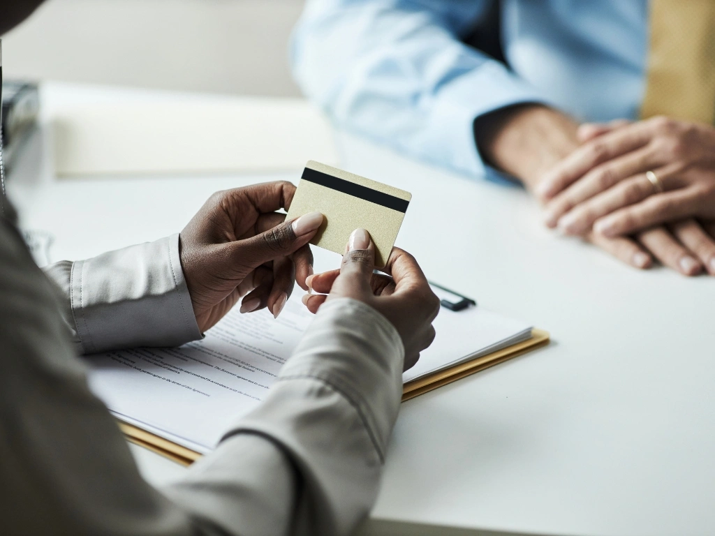 Close-up of a person holding a gold credit card over documents during a business meeting
