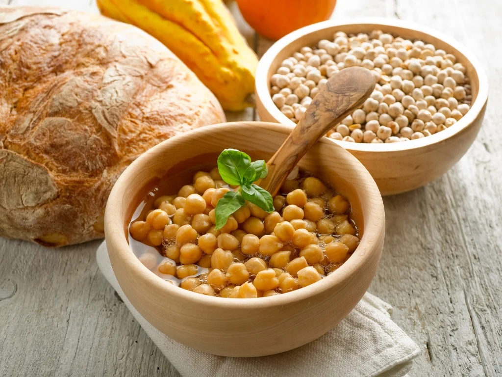 Wooden bowls of cooked and dried chickpeas next to a loaf of whole-grain crusty bread