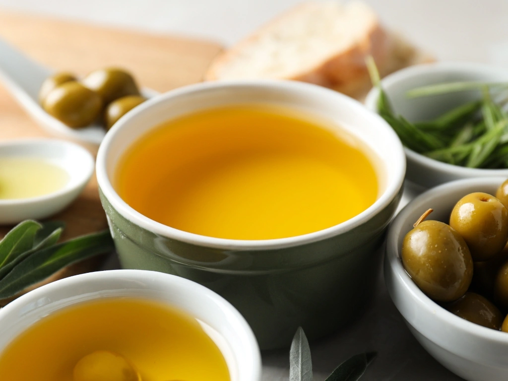 Small bowls of olive oil and green olives served with fresh herbs and sliced bread