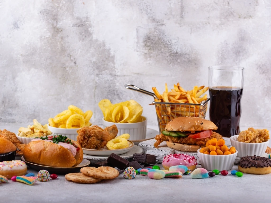 A spread of different foods to avoid with hyperthyroidism, including fast food, sugary desserts, and soda