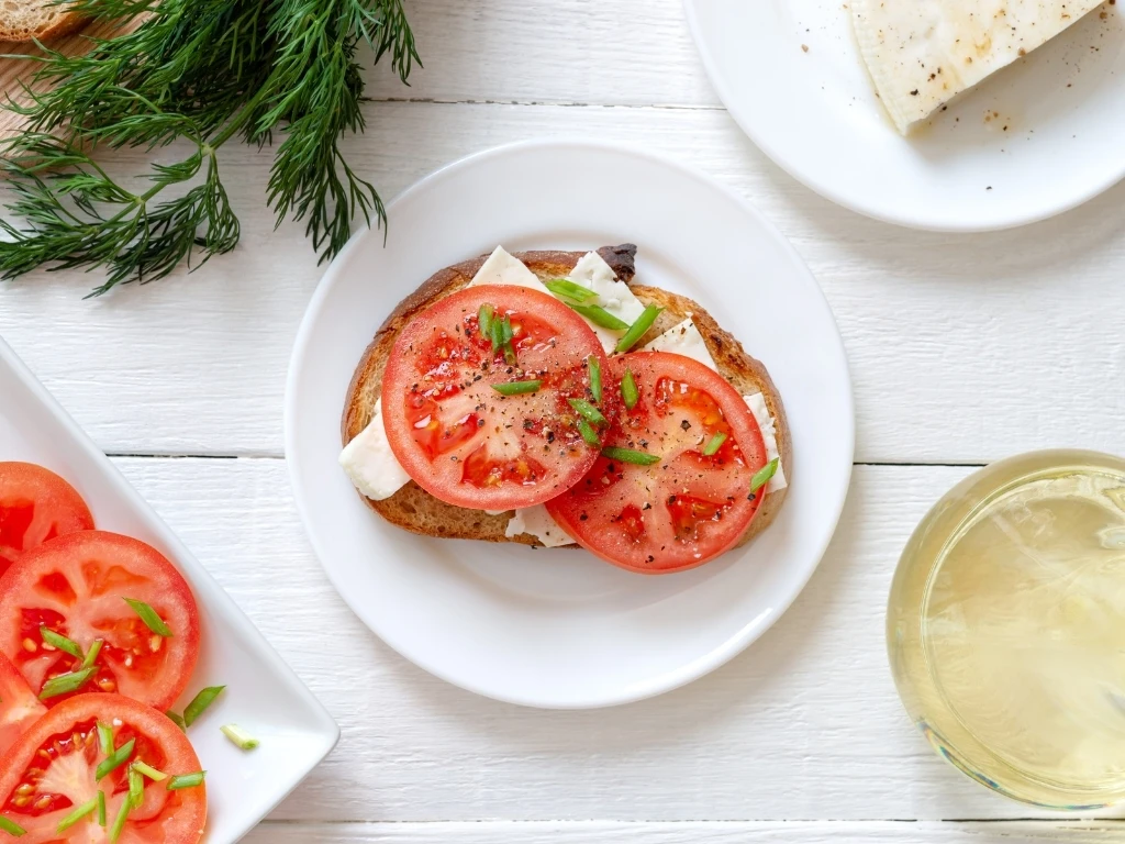 Whole grain bread with goat cheese and fresh tomatoes on white.